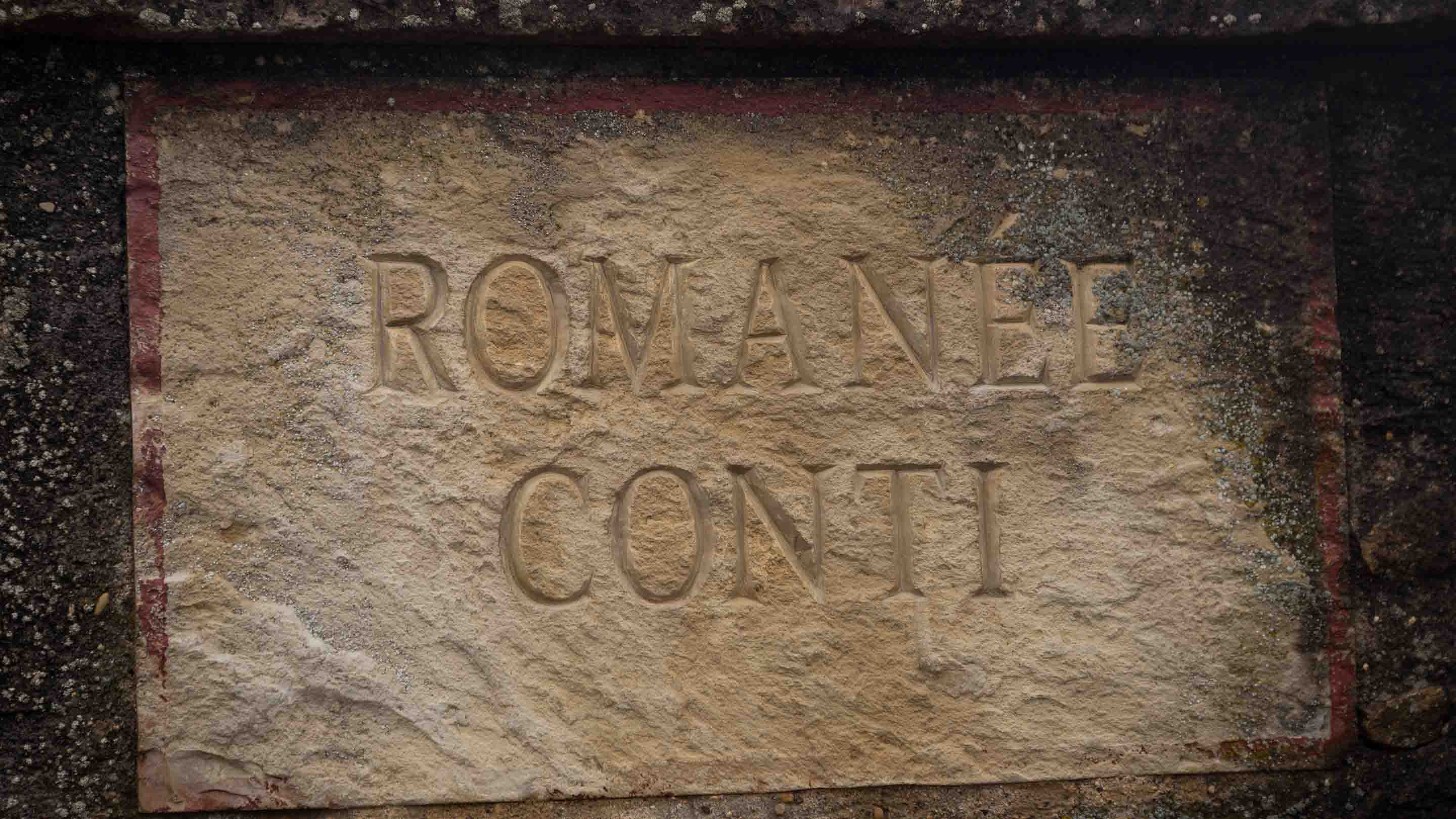 A stone sign engraved with the words ROMANEE CONTI. The background is textured and weathered, giving it an aged appearance.
